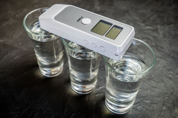 A breathalyzer laying across several glasses in alcohol